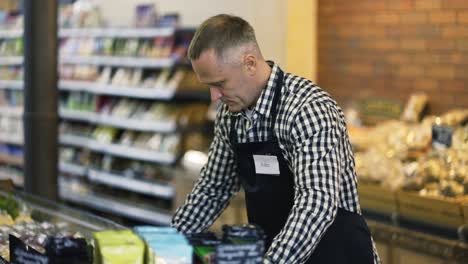 a middle-aged saleswoman in and apron brings exotic fruits in a box. the concept of working in a grocery store