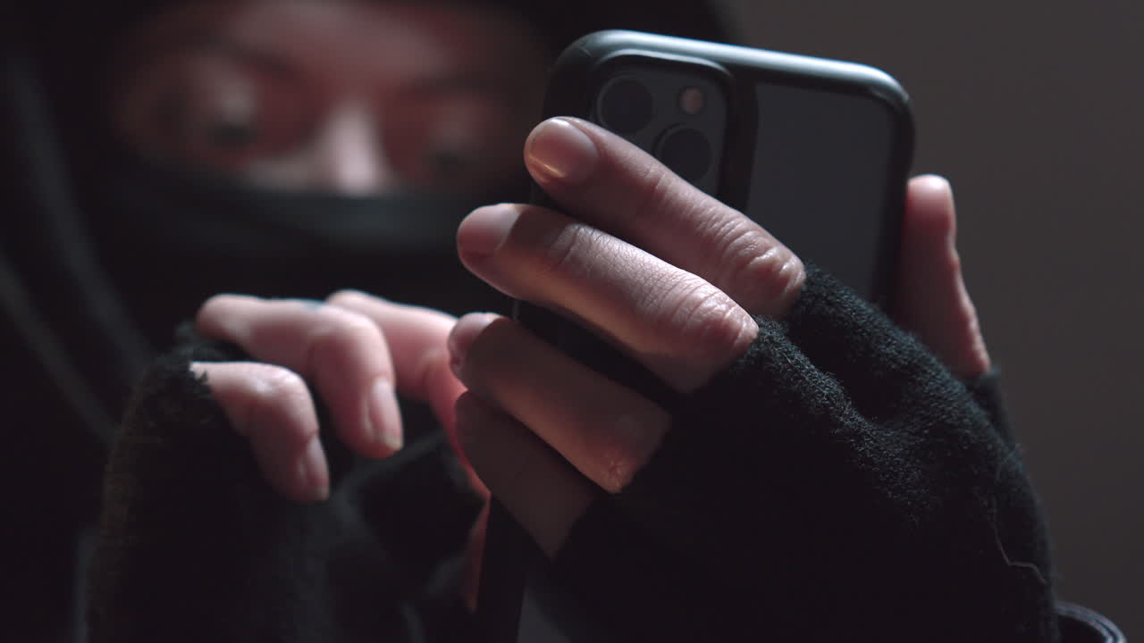 테러리스트 마스크를 쓴 사람이 휴대폰을 사용하고 주머니에 넣습니다.