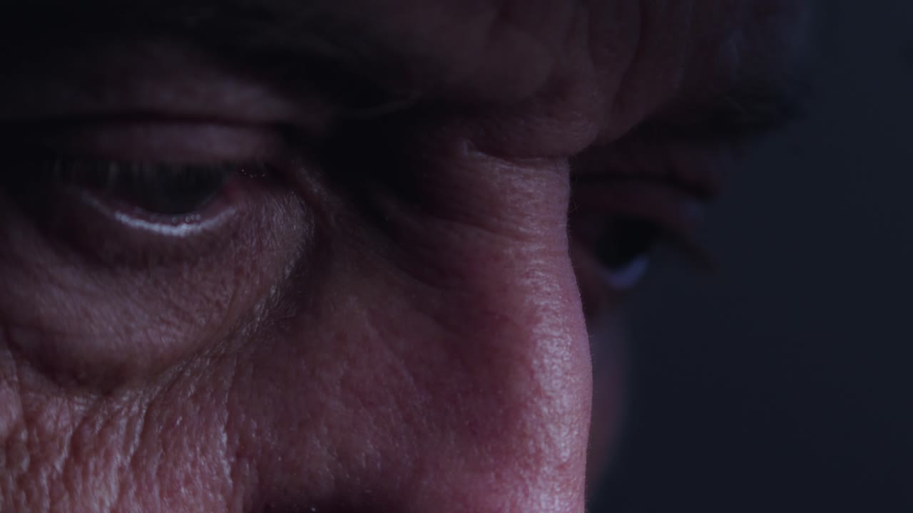 una mirada de cerca a los ojos de un anciano arrugado que está leyendo atentamente un documento en la atmósfera oscura de la habitación