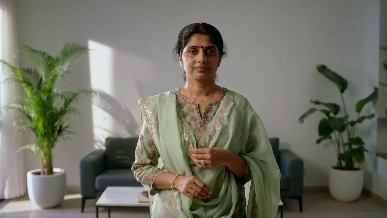Telecamera che zooma mostrando una donna indiana che liscia il dupatta e sistema il salwar kameez in salotto.