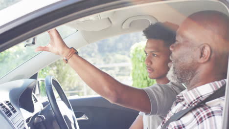 happy african american father instructing son about mirror in car before driving lesson, slow motion