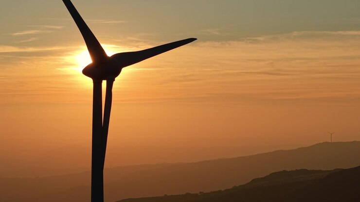 Hinterleuchtete Windturbinen als Silhouetten vor einem orangefarbenen Sonnenuntergang.