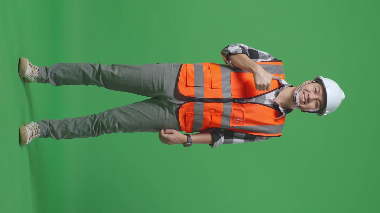 Full Body Of Asian Male Engineer With Safety Helmet Smiling And Showing Thumbs Up Gesture To The Camera While Standing In The Green Screen Background Studio