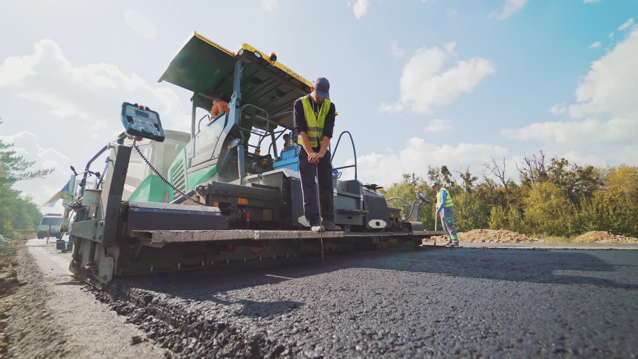Asphalt paver machine and workers during the road construction. Heavy machine for paving applying fresh asphalt. Man worker on the paver machine with special equipment.
