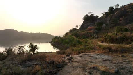 Aerial---Tracking-shot-of-two-men-on-a-bike-on-a-lonely-dirt-road-at-sunset