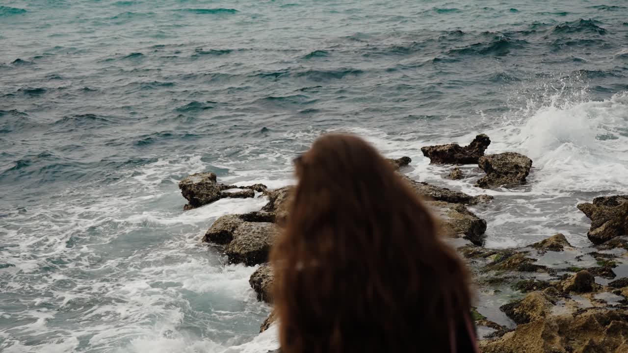 Woman looks at ocean waves splashing over rocky shore in Tangier, Morocco
