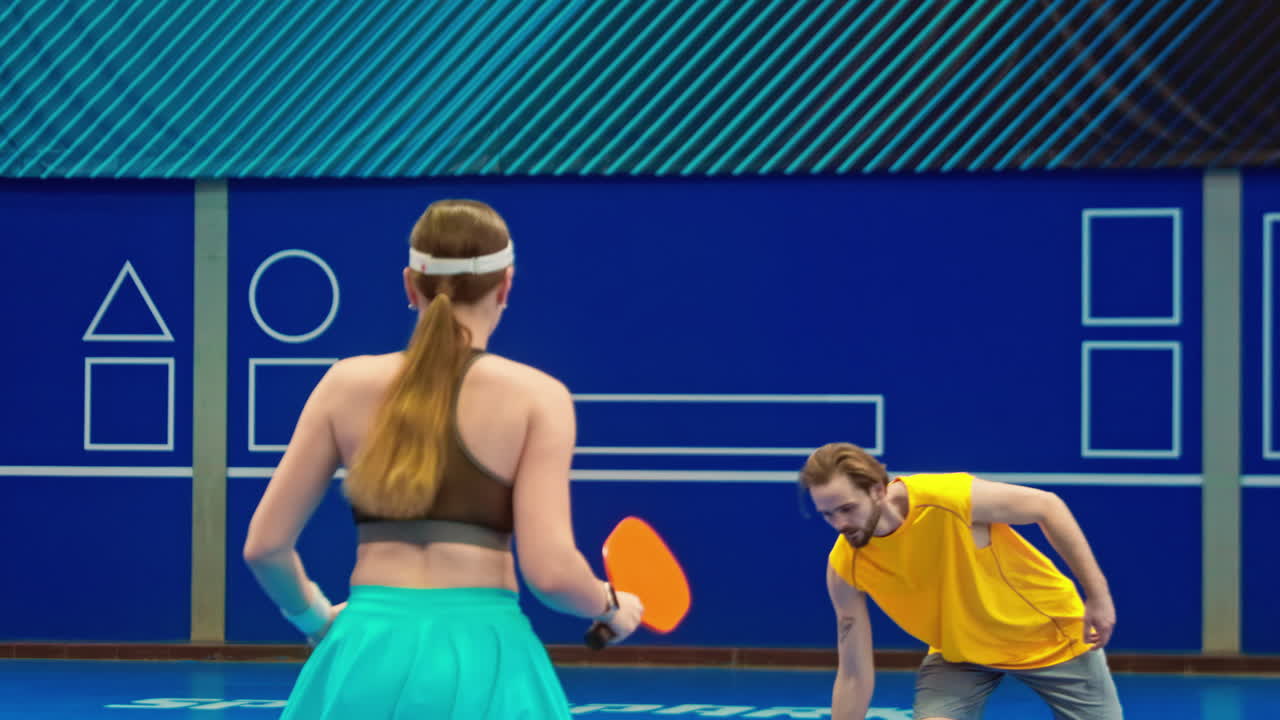 A man and a woman playing pickleball on a blue, inside court