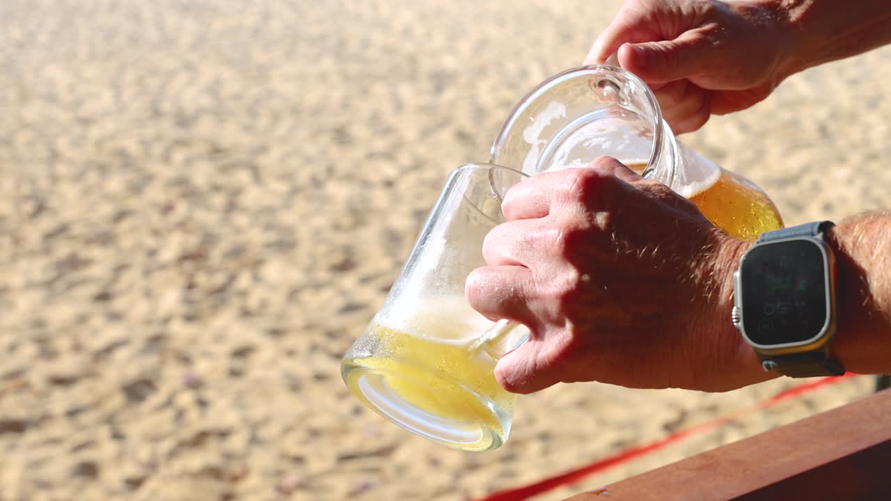 Manos sirviendo cerveza de una jarra en la playa.