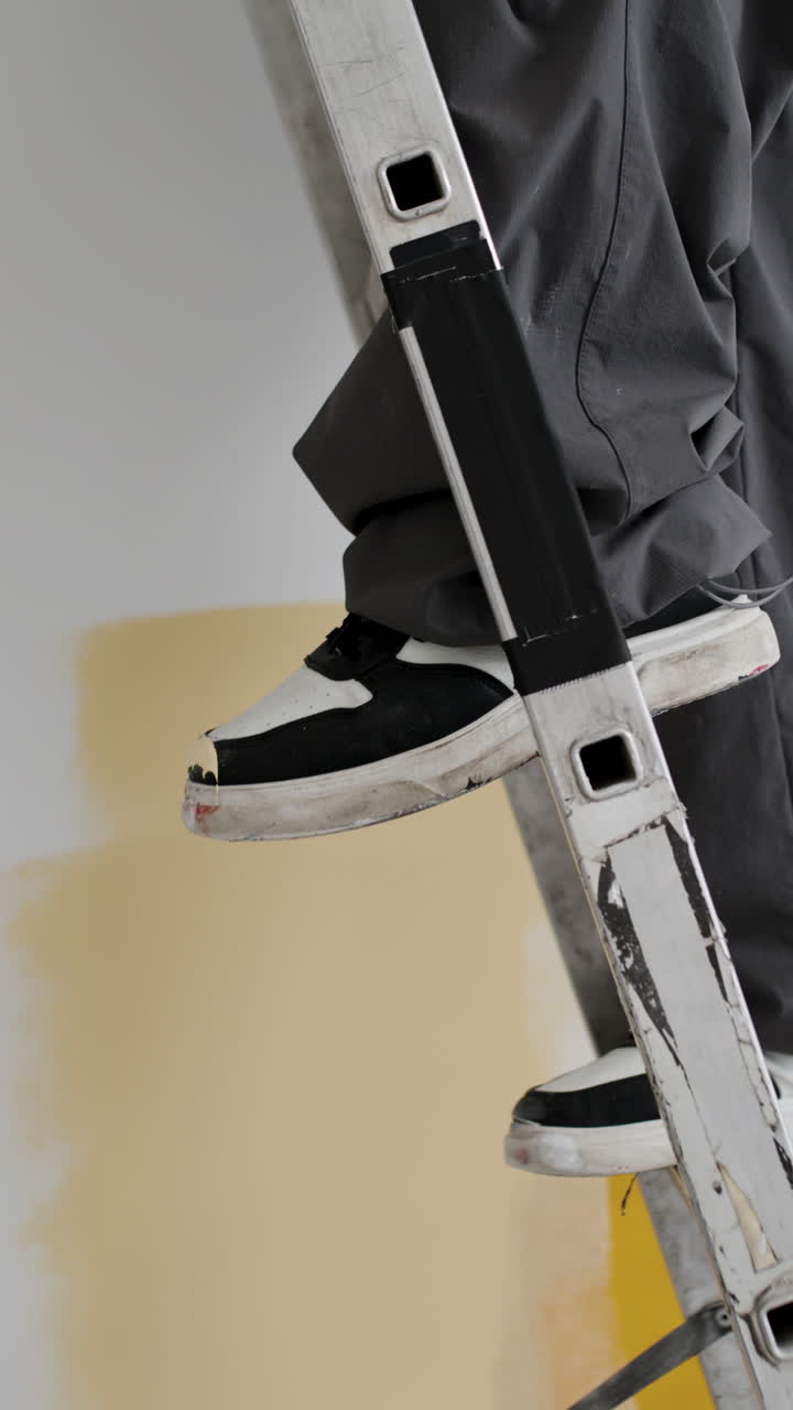 Man Climbing a Ladder While Painting a Wall