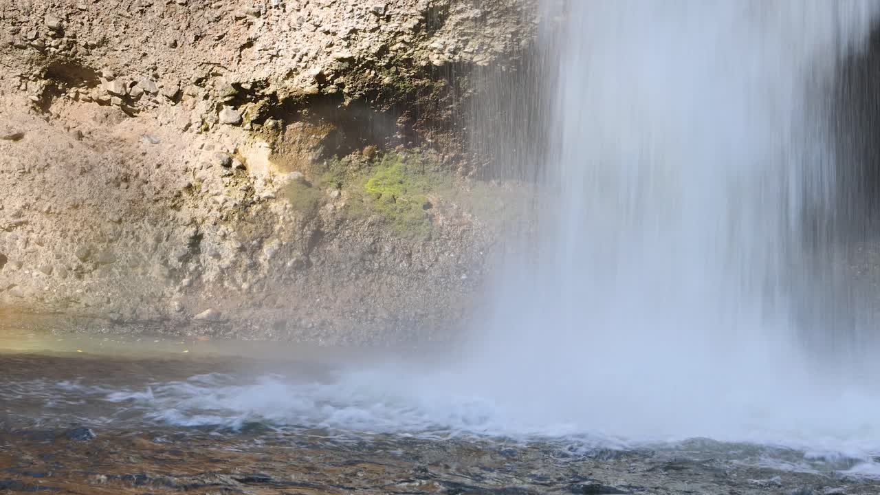 Steady waterfall cascades over mossy rocks, bright daylight, fixed camera, soft flowing water