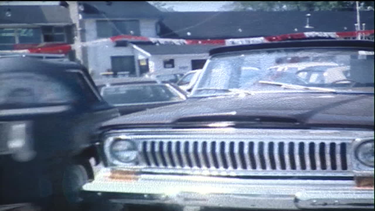 Camera walks along in front of a row of 1970's jeep trucks on a car lot at an auto dealership