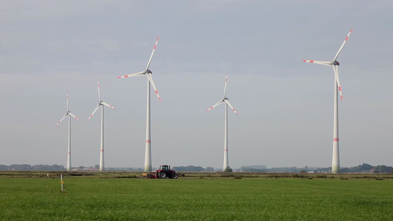 풍력 터빈이 우뚝 솟은 밭을 갈고 있는 트랙터