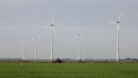 a tractor ploughing a field, with wind turbines towering over it