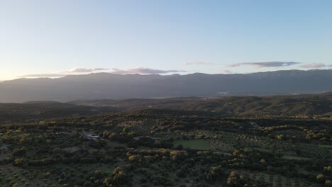 aerial-flight-with-a-drone-in-a-valley-in-Spain-over-a-forest-of-native-trees-of-the-country-making-a-gentle-turn-to-the-left-on-a-sunset,-with-a-beautiful-background-of-mountains