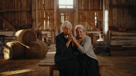 Two elderly women praying together in a barn