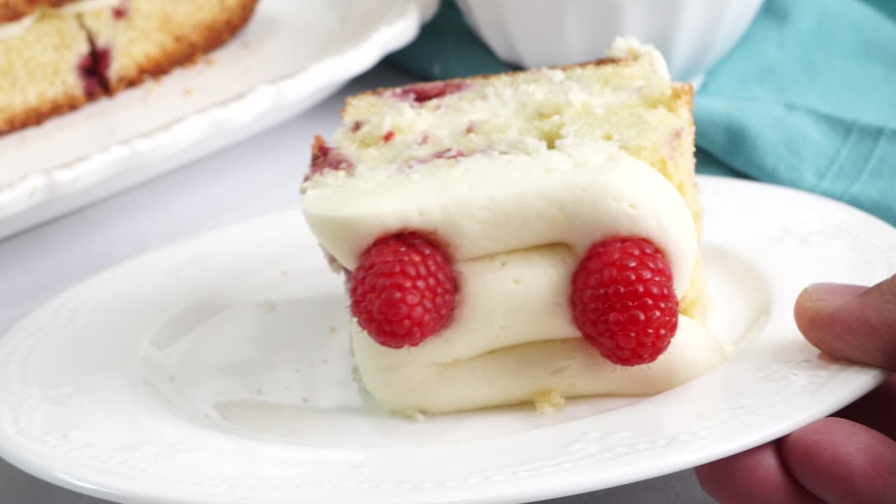 Making a dessert called Red Raspberry Tea Cake made with fresh berries and vanilla buttercream frosting. Great for Tea Parties. Close up of a piece of raspberry tea cake on a white plate