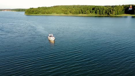 motor boat driving on a lake surrounded by a forest during summer in brandenburg, germany