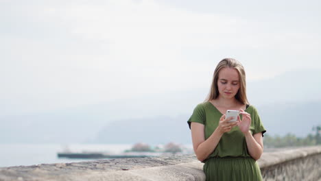mujer en teléfono inteligente gadget en la costa de arena. viajero usando en mano femenina móvil en el fondo playa paisaje marino horizonte. vista turística en el sol azul océano, estilo de vida de verano
