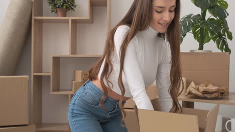 Mujer-Sentada-En-El-Suelo-Cerrando-Una-Caja-De-Cartón-Y-Sonriendo-A-La-Cámara