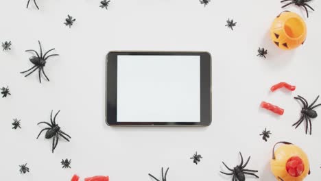 Candies-in-scary-halloween-pumpkin-printed-bucket,-spider-toys-and-digital-tablet-on-grey-background