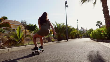 Zeitlupe-Fängt-Die-Schönheit-Eines-Jungen-Mädchens-Ein,-Das-Mühelos-Auf-Seinem-Longboard-Eine-Strandstraße-Mit-Palmen-Entlang-Gleitet