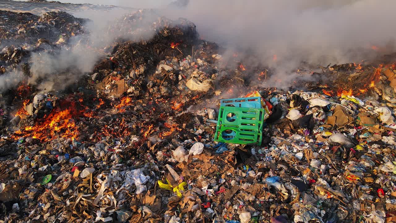 Flames consume plastic waste as thick smoke rises from smoldering landfill surface