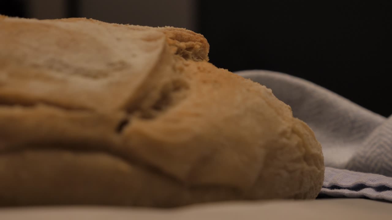 Slow motion pan into freshly baked loaf of sour dough bread topped with flour sitting on kitchen bench with tea towel and tray, low depth of field
