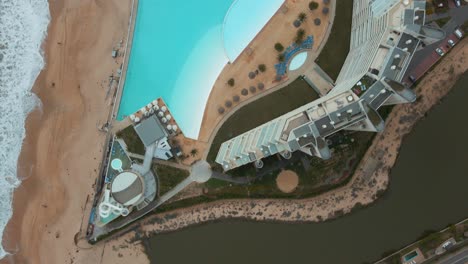 Aerial-top-down-dolly-in-of-turquoise-world-largest-swimming-pool-near-sea-shore-and-resorts,-Algarrobo,-Chile