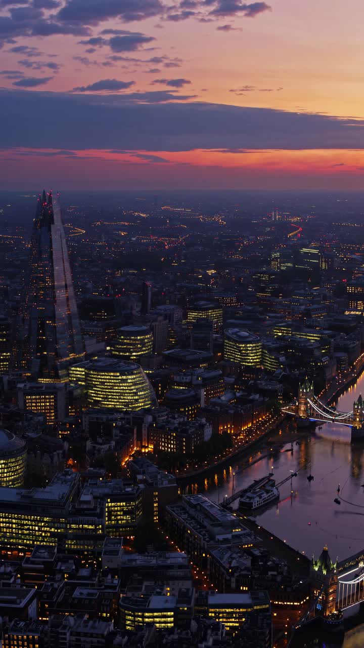 Aerial video view of a cityscape at dusk, showcasing illuminated buildings and a river