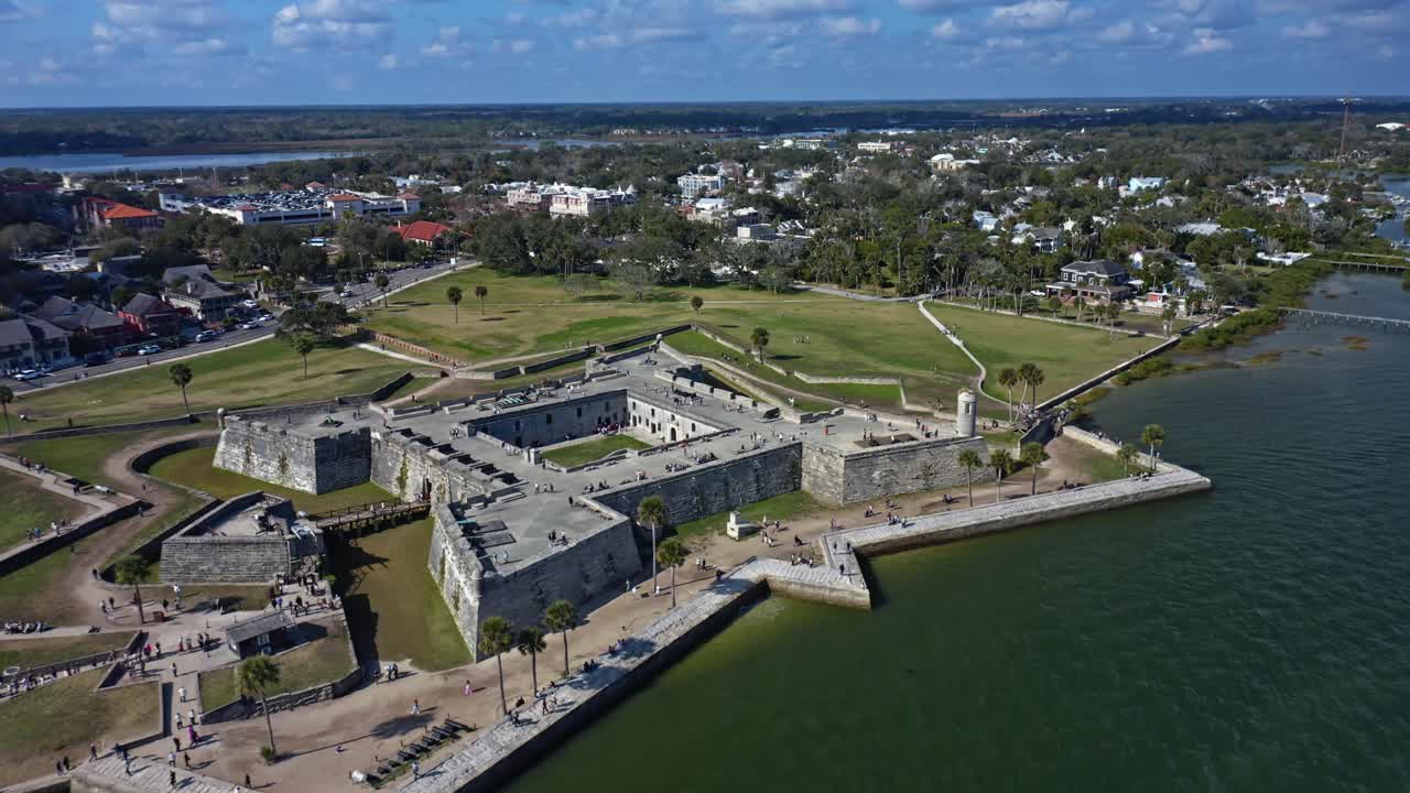 Historic Castillo de San Marcos fortress sits on St. Augustine's waterfront surrounded by grassy park areas and nearby streets lined with residential homes and small buildings