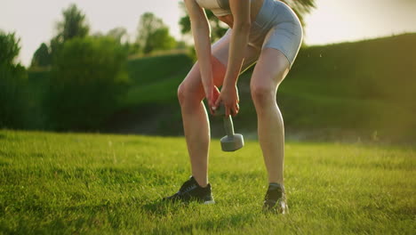 A-woman-squats-with-dumbbells-in-the-Park-at-sunset-lifting-dumbbells-in-front-of-her.-Training-with-weights.-Motivation