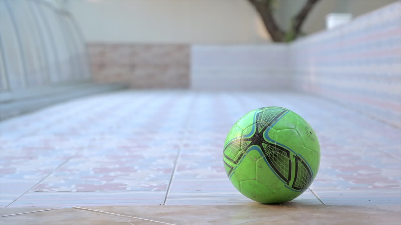 Boy kicking a green football in a courtyard