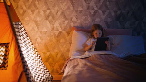 smiling kid surfs internet on tablet in comfortable bed