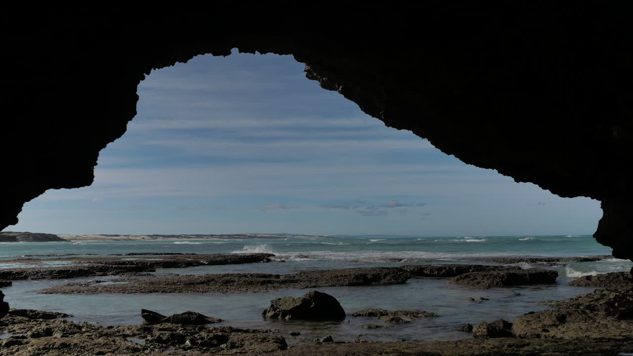 vista desde una pequeña cueva en la costa rocosa de olas corriendo hacia la orilla, toma estática