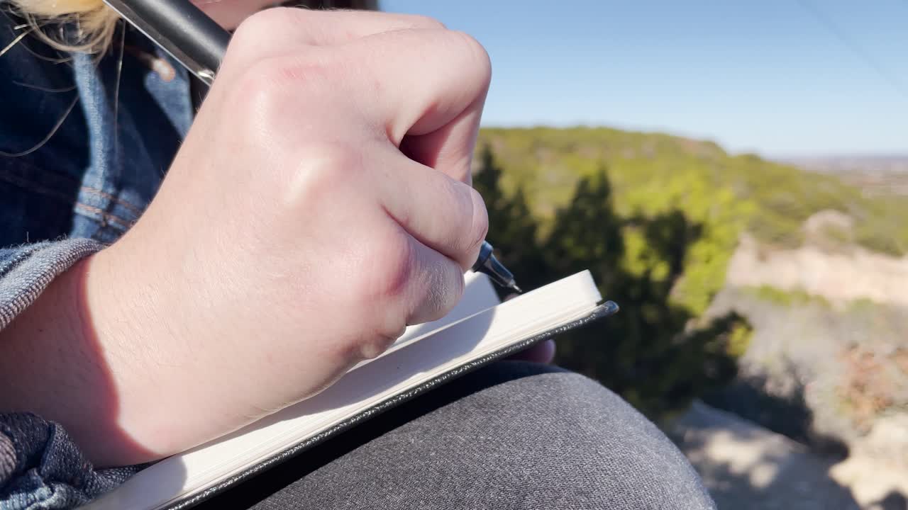Primo piano di una ragazza che prende appunti su un quaderno su una montagna in estate