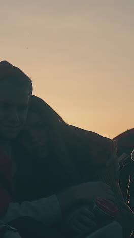 group of young friend tourist silhouettes sits in cozy camp on meadow in autumn evening at back sunset slow motion