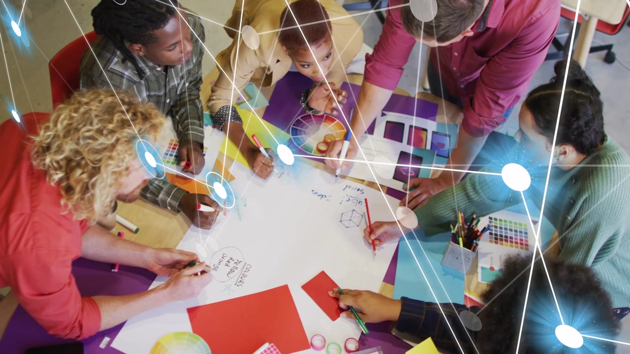 Design team leaning over round table spreading swatches, forming overlay linking nodes across sheet