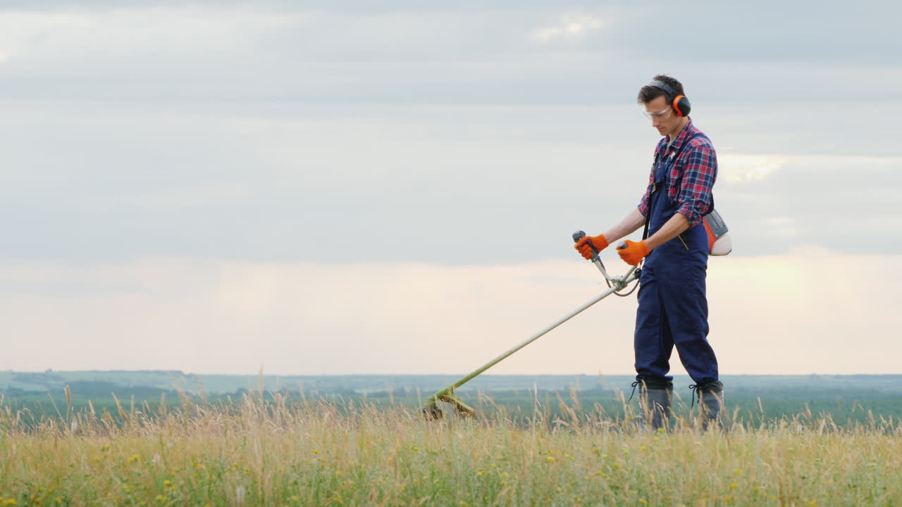 그림 같은 초원에서 트리머로 잔디를 깎고 있는 청년