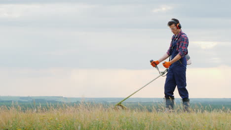 young man mowing grass with a trimmer on a picturesque meadow