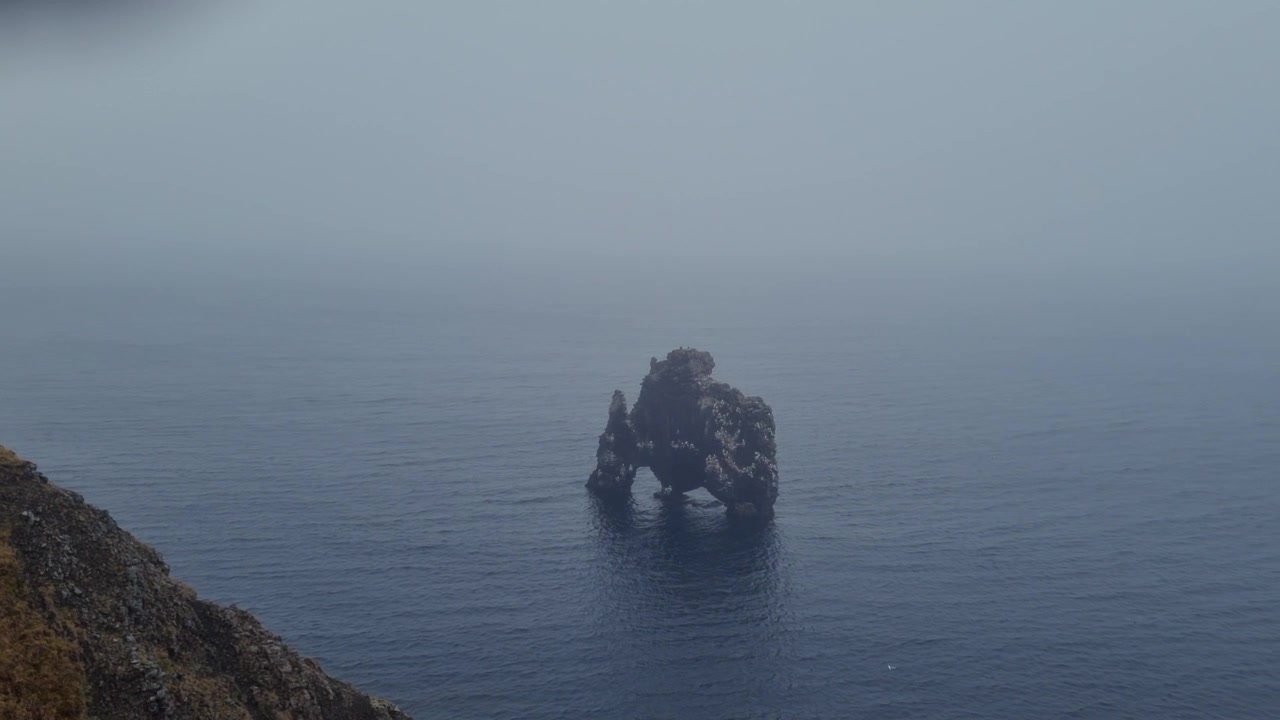 Turista observando la pila de roca basáltica Hvitserkur en Islandia desde un mirador en un día frío y con niebla, mostrando el majestuoso paisaje
