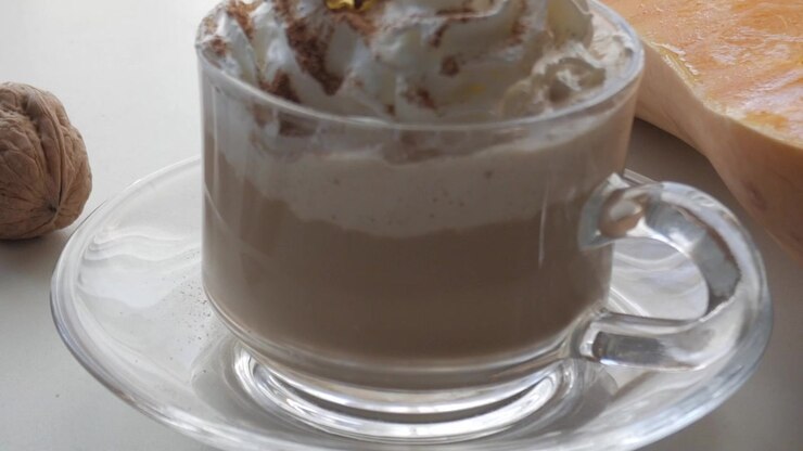 Spezie e noci disposte su un tavolo accanto a un bicchiere di caffè, che suggeriscono accoglienti sapori autunnali.