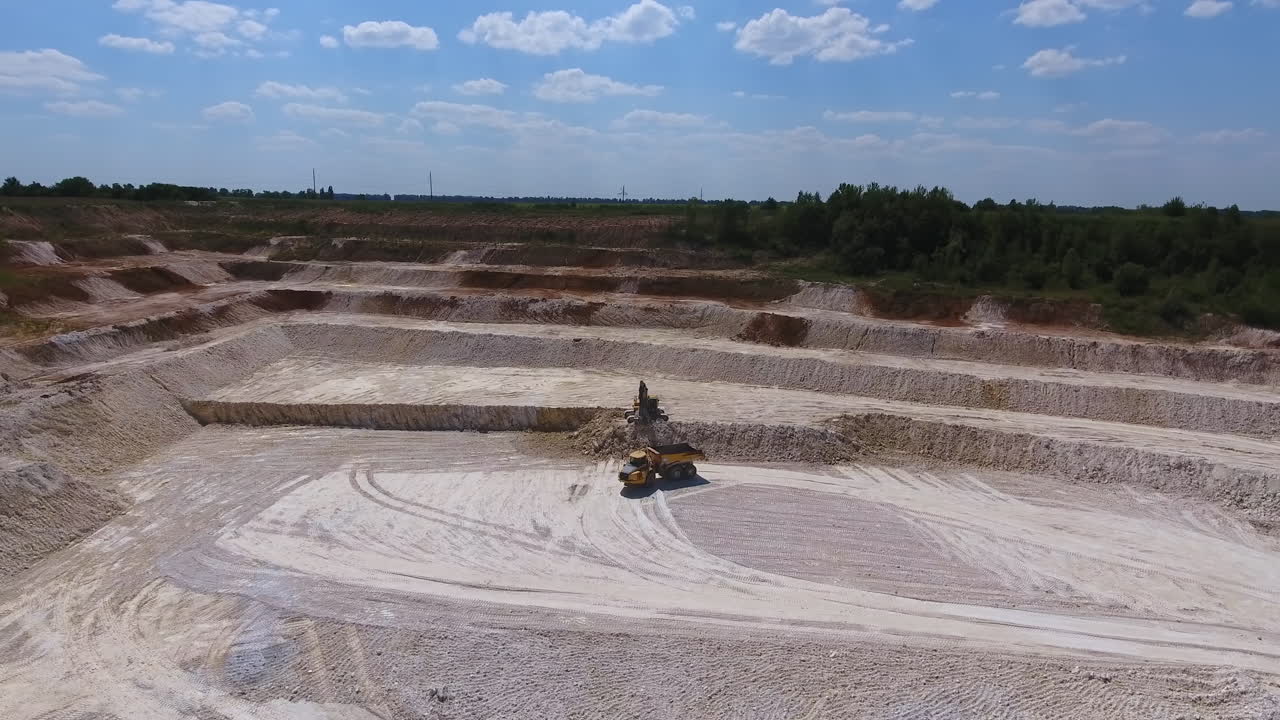 Straight ground at the kaolin quarry. Excavator machine digging the rock formations. Lorry approaching to be uploaded with minerals.