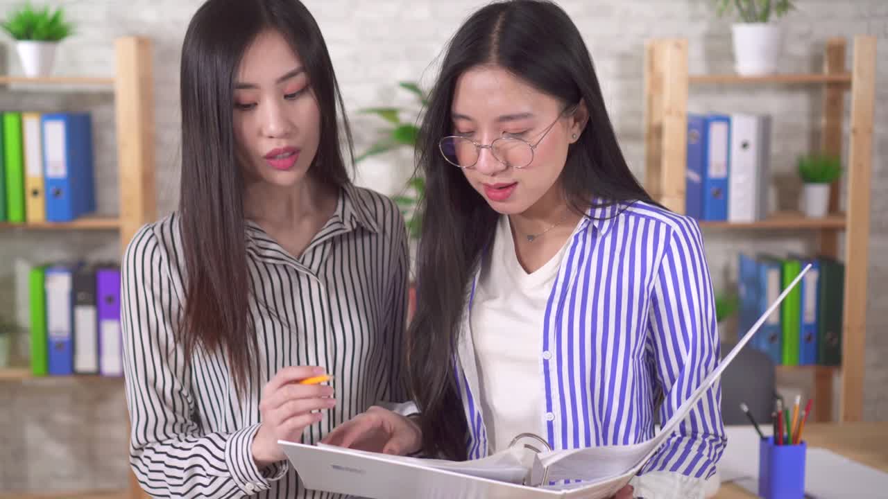 Two young asian girls office workers discuss documents in the office close up