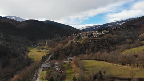 aerial: approaching a little mountain town in a mountainous landscape with snow covered mountains in the background