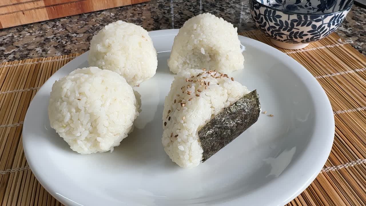 Un piatto di onigiri appena fatti viene servito, con uno guarnito con semi di sesamo e alghe - Primo piano.