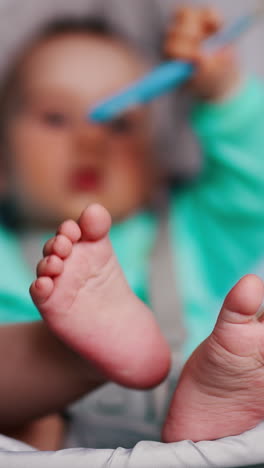 tiny feet of an infant sitting in a baby chair. cute child pulls spoon into mouth. blurred backdrop. vertical video