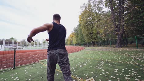 male fitness sportsman training his body on the stadium. muscular man dressed in black shirt exercises on autumn background. slow motion. healthy lifestyle.