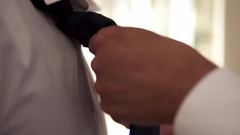 slow motion handheld close up shot of groom getting ready for his wedding with bride and having his tie tied on wedding day