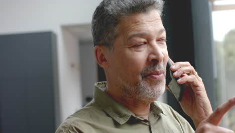 hombre de dos razas hablando en teléfono inteligente, mirando por la ventana en casa, espacio de copia, cámara lenta