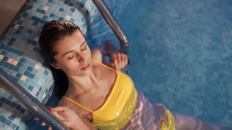 retrato de una linda joven con un traje de baño amarillo en la piscina sonriendo